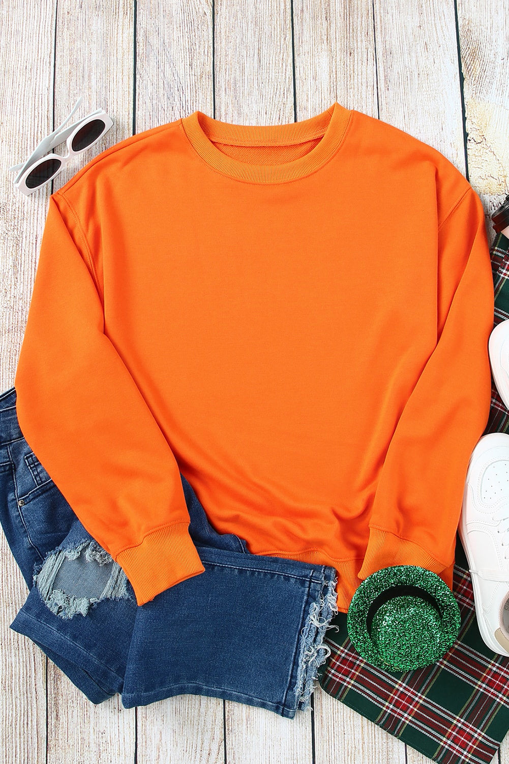 Person with wavy, shoulder-length hair wearing an Orange Plain Crew Neck Pullover Sweatshirt and blue jeans, standing with hand on hip, facing away.