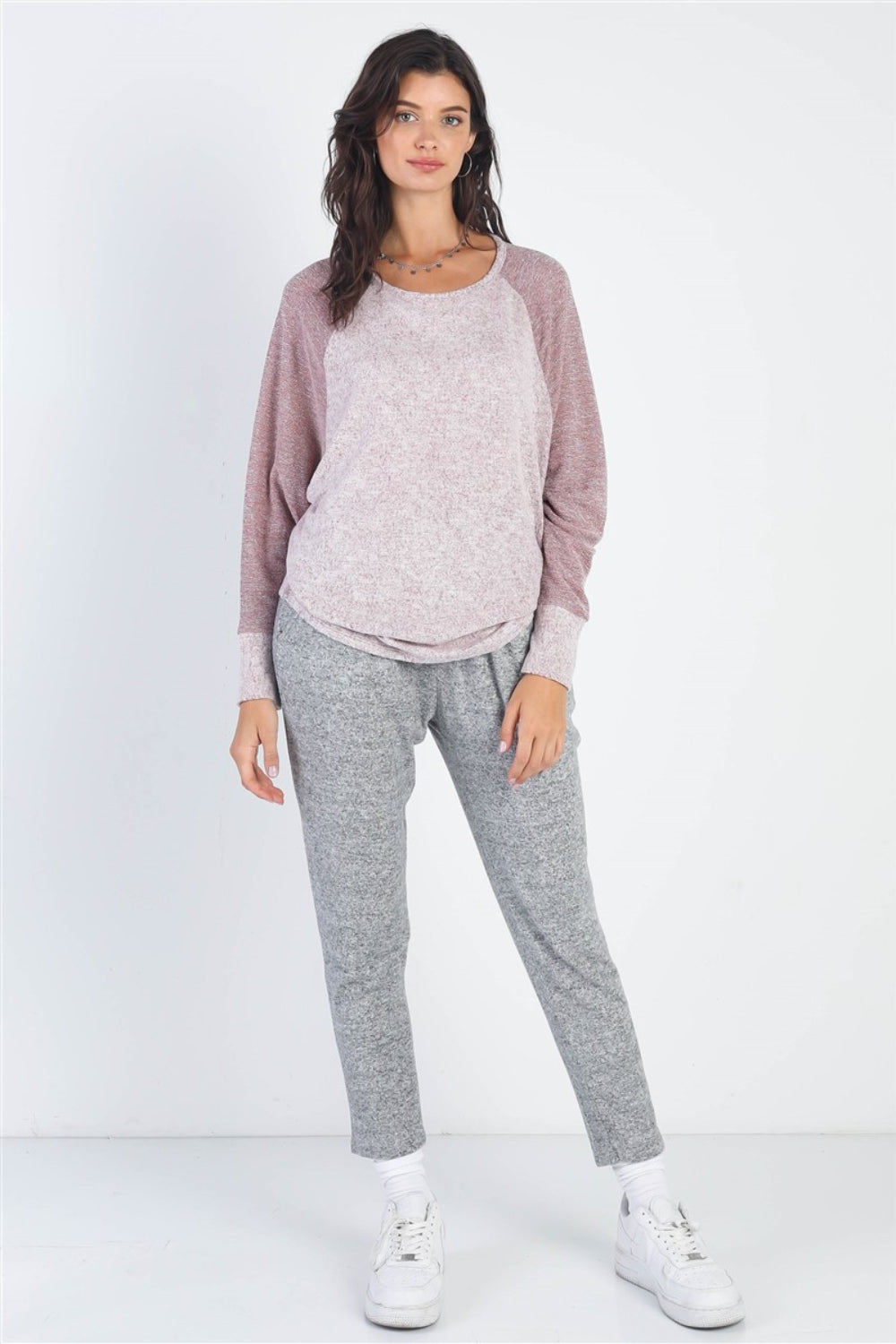 A woman stands wearing the Cherish Apparel Round Neck Long Sleeve Contrast Top in pink and gray with matching gray pants, set against a plain background.