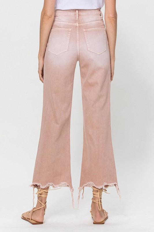 Person wearing 90's Vintage Crop Flare Jeans in rose pink with high waist, distressed details, rips on the knees, and frayed hems, paired with beige strappy sandals.