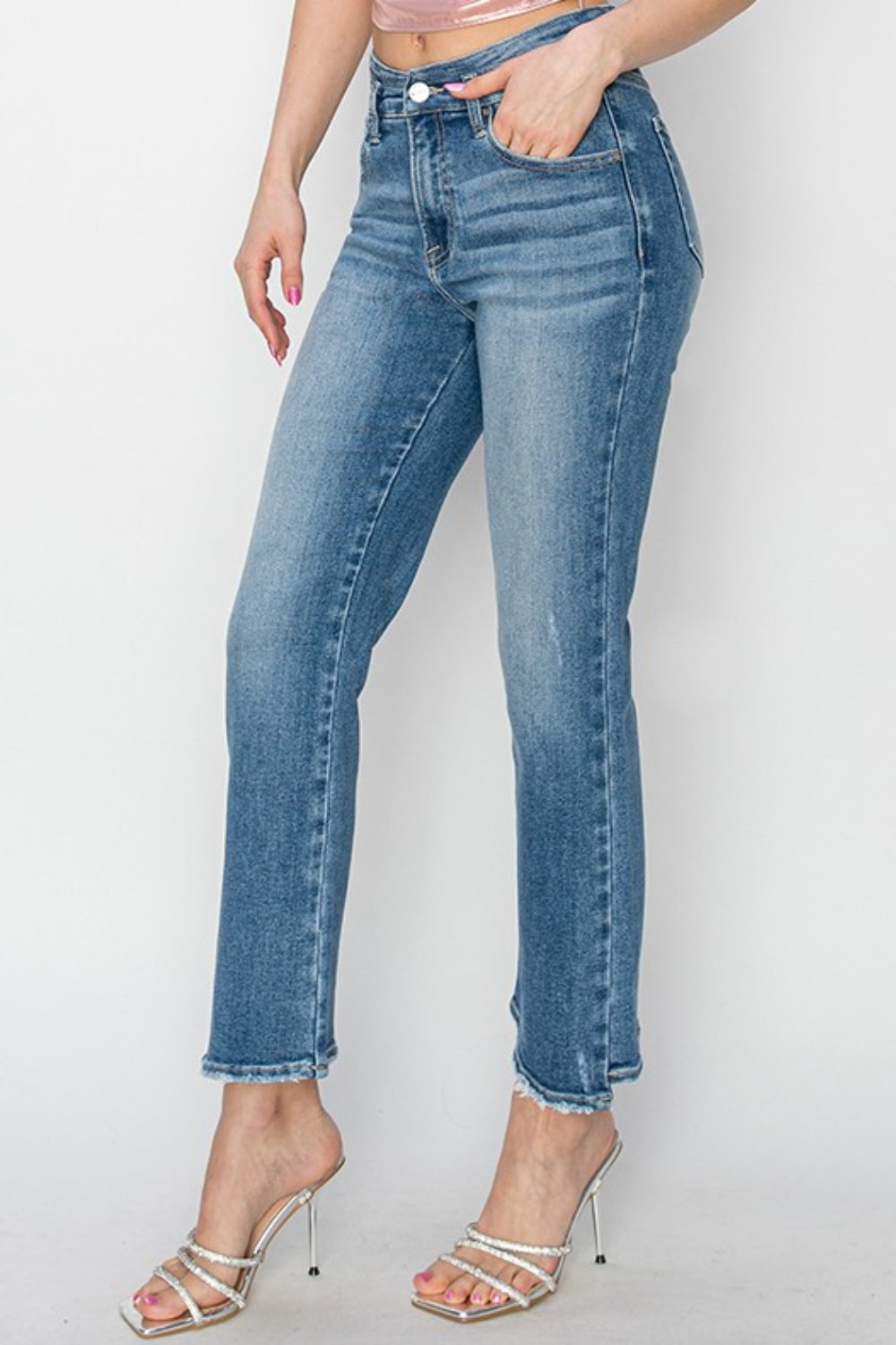 A person wearing RISEN High Rise Slim Straight Jeans with frayed hems and open-toe high-heeled sandals adorned with pearl details, standing against a plain white background.