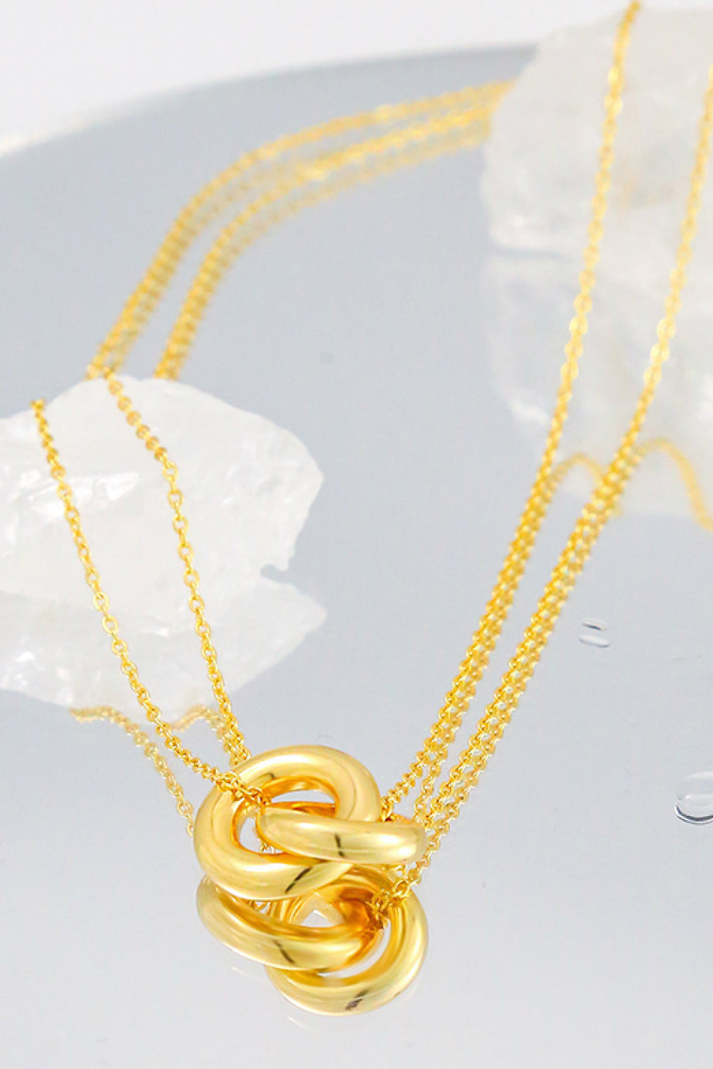 The Linked Ring Pendant Chain Necklace showcases an elegant design with a gold pendant featuring two interlocking circles.