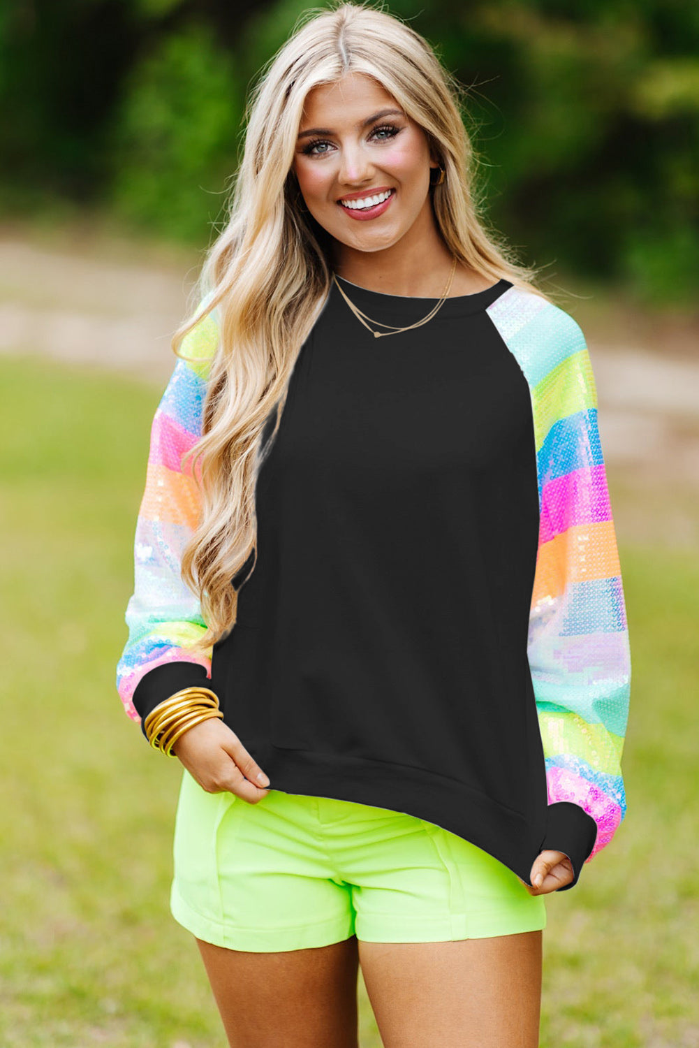 A person with shoulder-length hair is wearing a Black Sequin Color Block Raglan Sleeve Pullover Sweatshirt and blue jeans. They are facing away from the camera in a room with a potted plant.