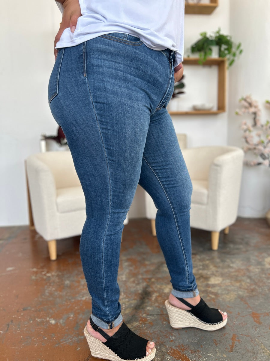 Person wearing Judy Blue Full Size Cuffed Hem Skinny Jeans and a white T-shirt, posing with one hand in pocket and feet in black open-toe shoes.