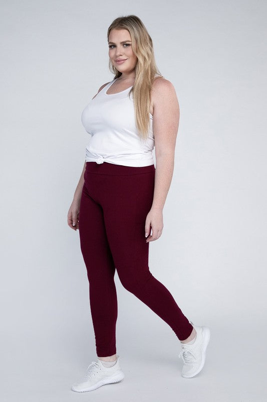 A person with long hair in casual attire is wearing a white t-shirt, Plus Everyday Leggings with Pockets in black, and white sneakers. They are holding a white cap and sporting a black crossbody bag.