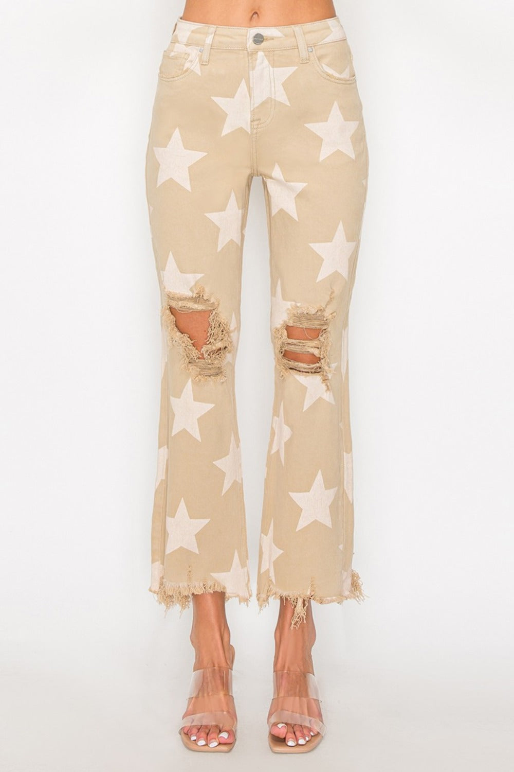 Someone dressed in RISEN Full Size High Rise Star Printed Frayed Hem Jeans with ripped knees, complemented by clear heels.