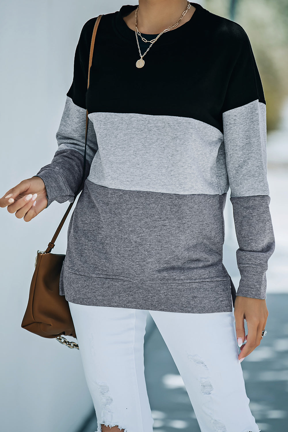 A person wearing a Colorblock Black Contrast Stitching Sweatshirt with Slits featuring black, gray, and light gray stripes, paired with white pants that resemble leggings and carrying a brown bag, shown from behind.