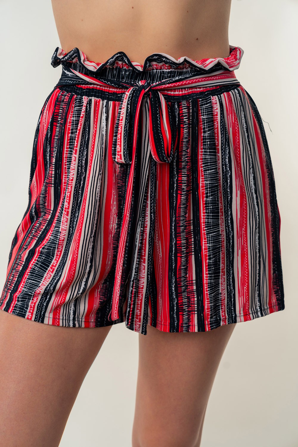 A person wearing the White Birch Full Size High Waisted Striped Shorts in red, black, and white, made from lightweight fabric and featuring a tie-front waistband.