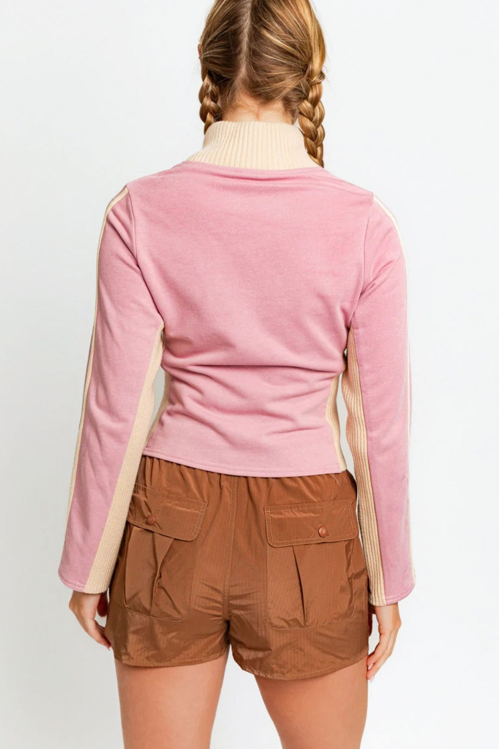 A person wearing the Le Lis Long Sleeve Mock Neck LONDON Embroidered Jacket in light pink and brown pants, looking to the side.