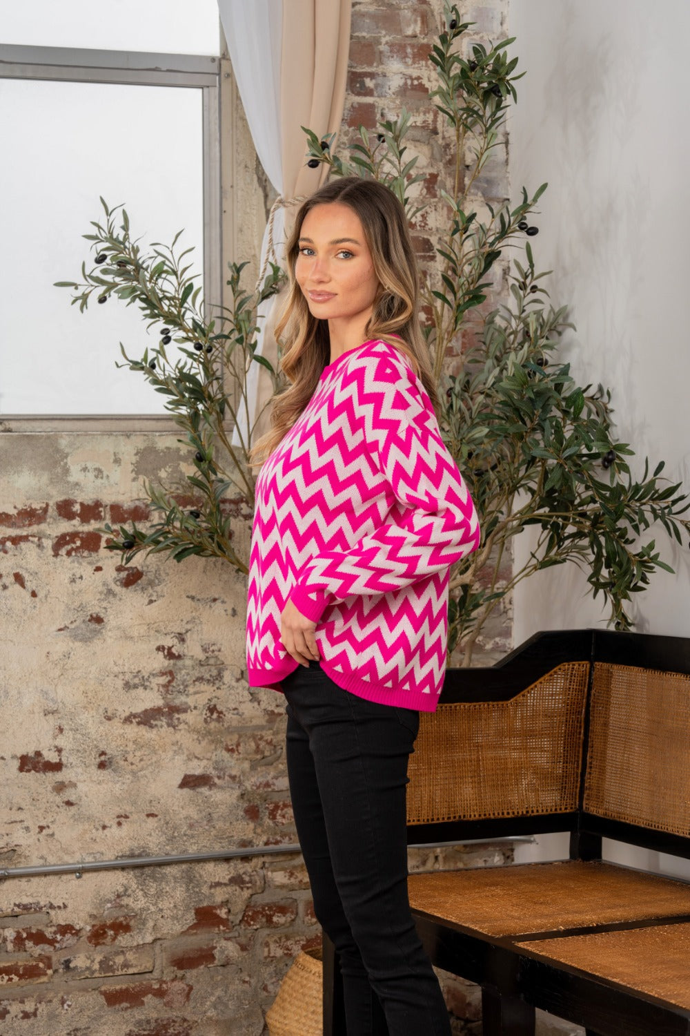 A person wearing the Sew In Love Full Size Wave Stripe Contrast Long Sleeve Sweater stands indoors near a potted plant and a brick wall.