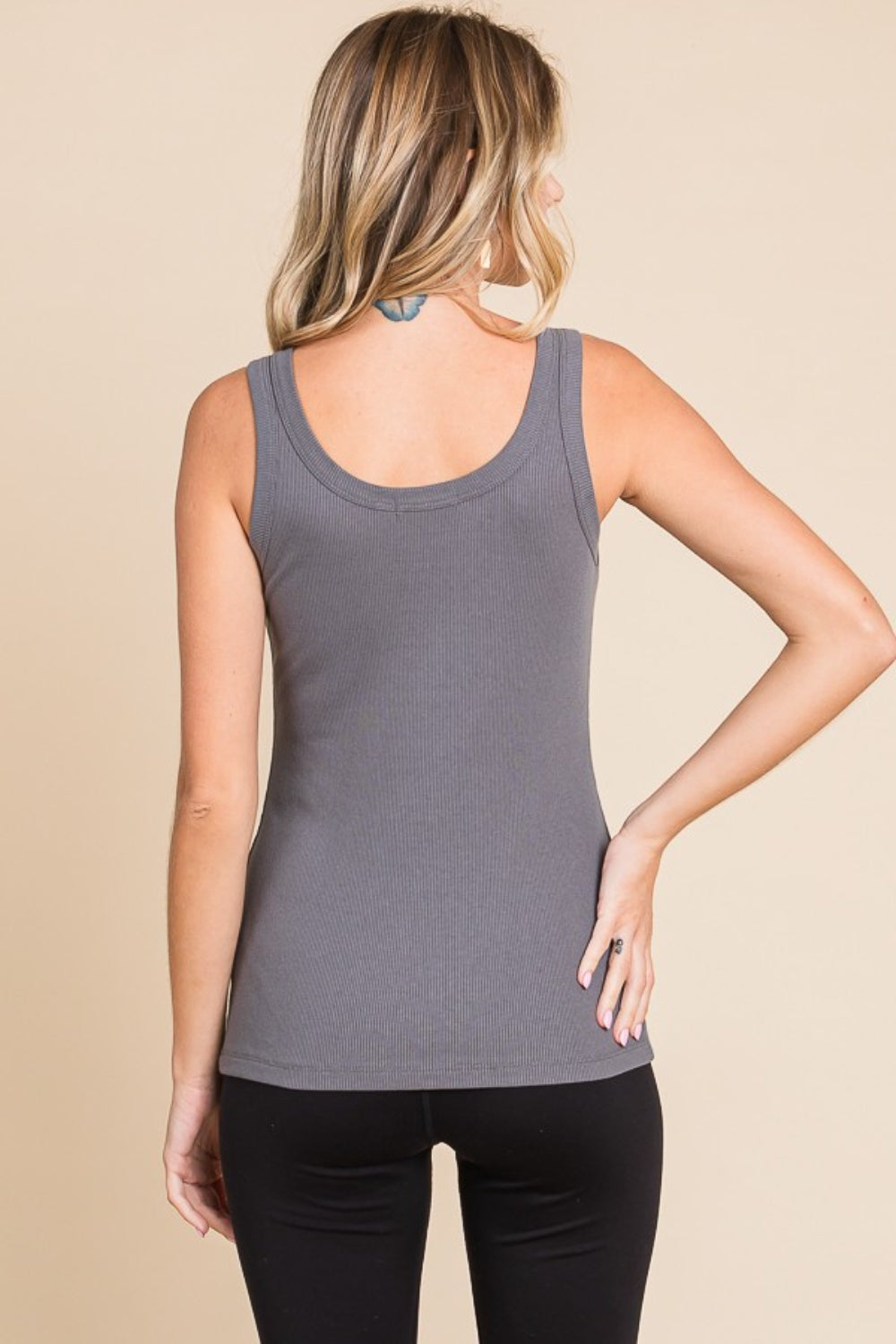 A person wearing a versatile wardrobe staple—a Culture Code Full Size Ribbed Scoop Neck Tank—and black pants stands against a beige background.