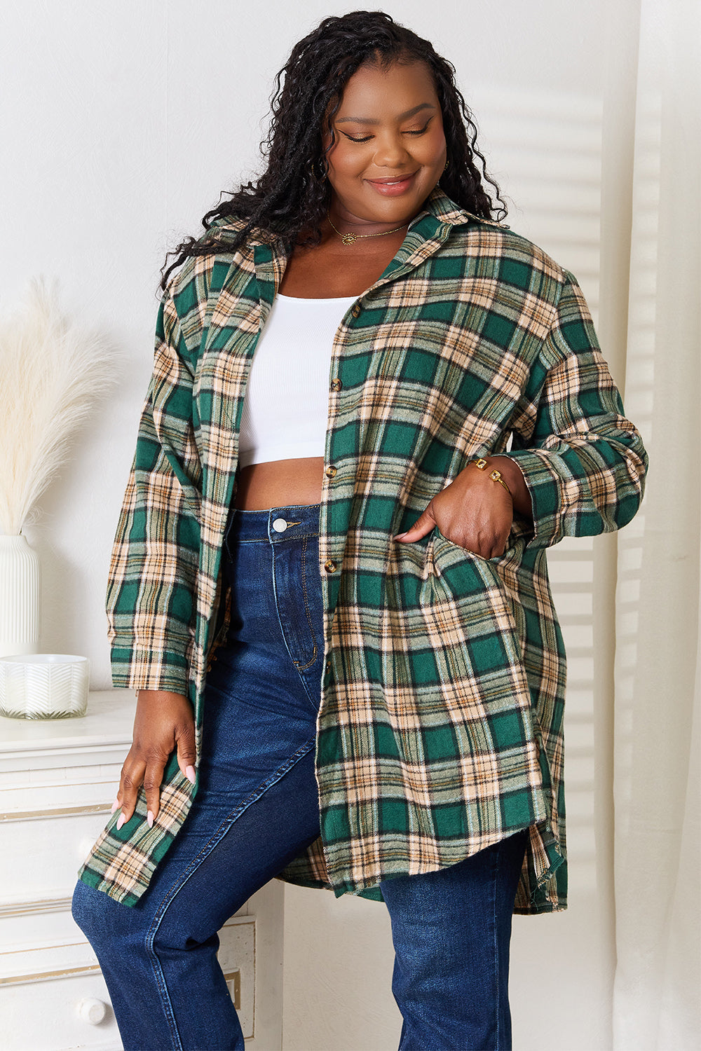 A person wearing the Mandy Plaid Collared Neck Long Sleeve Shirt in green and beige over a white crop top and blue jeans, standing indoors near a white dresser with vases.