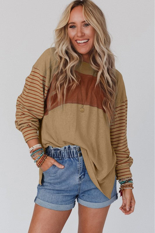 A woman wearing a Color Block Stripe Lantern Sleeve Side Slit Tunic with denim shorts, accessorized with layered necklaces for a touch of sophistication.