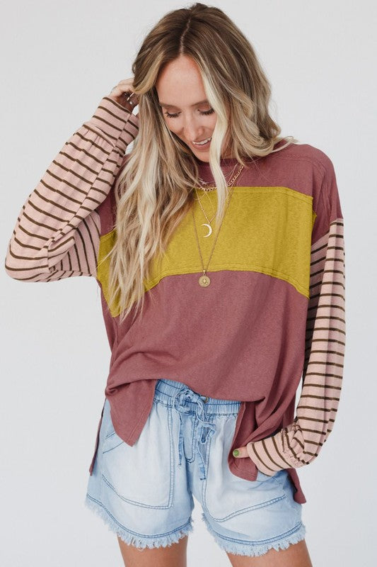 A woman wearing a Color Block Stripe Lantern Sleeve Side Slit Tunic with denim shorts, accessorized with layered necklaces for a touch of sophistication.