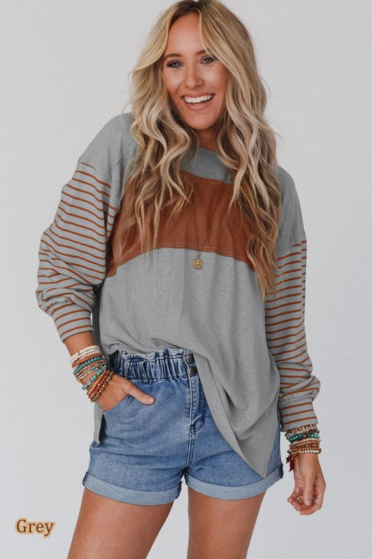 A woman wearing a Color Block Stripe Lantern Sleeve Side Slit Tunic with denim shorts, accessorized with layered necklaces for a touch of sophistication.