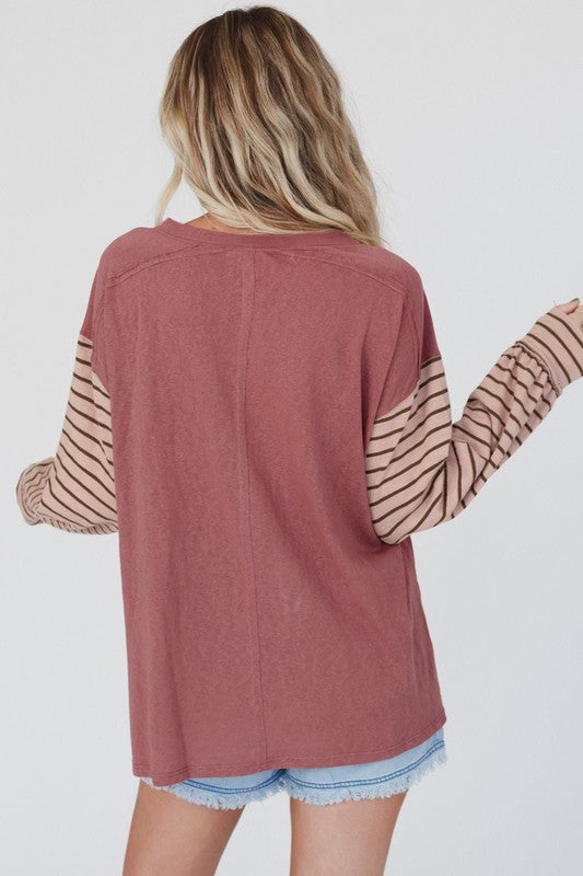 A woman wearing a Color Block Stripe Lantern Sleeve Side Slit Tunic with denim shorts, accessorized with layered necklaces for a touch of sophistication.