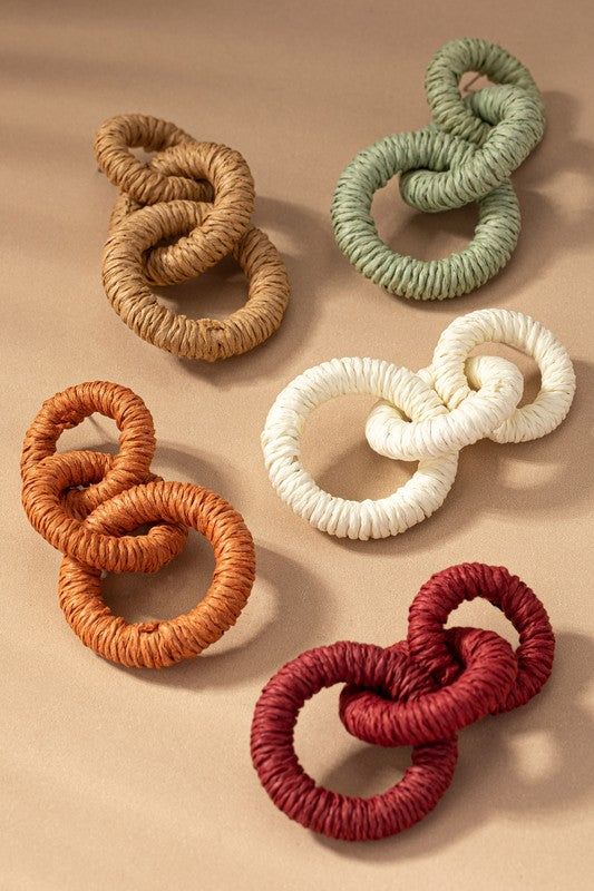 The Hemp rope wrapped chunky wood hoop earrings, featuring a delightful mix of beige, green, orange, white, and red hues, gracefully displayed on a tan surface evoke the stylish essence of Fall 23 colors.