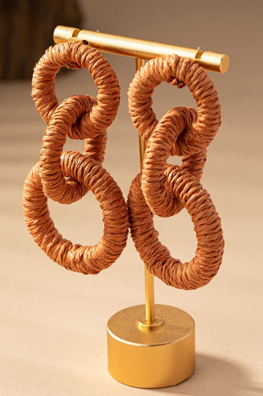 The Hemp rope wrapped chunky wood hoop earrings, featuring a delightful mix of beige, green, orange, white, and red hues, gracefully displayed on a tan surface evoke the stylish essence of Fall 23 colors.