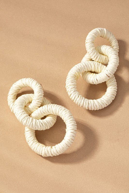 The Hemp rope wrapped chunky wood hoop earrings, featuring a delightful mix of beige, green, orange, white, and red hues, gracefully displayed on a tan surface evoke the stylish essence of Fall 23 colors.