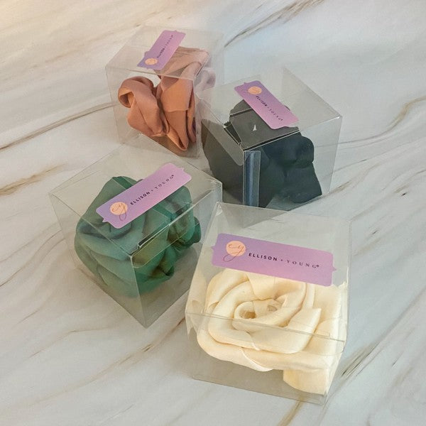 Four high-quality Art Of Work Satin Rose Scrunchies in black, pink, green, and cream arranged on a marble surface.