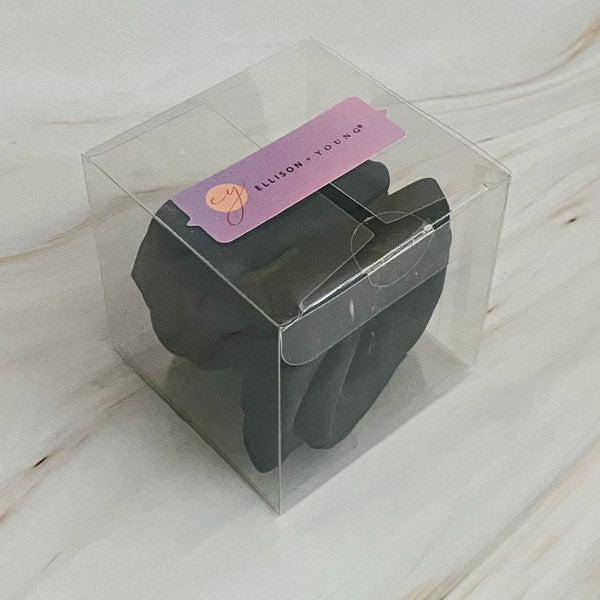 Four high-quality Art Of Work Satin Rose Scrunchies in black, pink, green, and cream arranged on a marble surface.