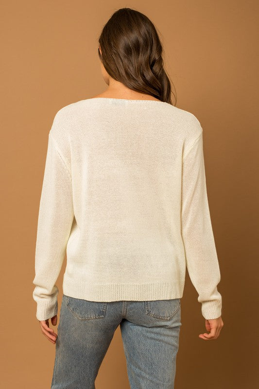 Wearing a Round Neck Long Sleeve Sea Salt Sun Sweater, beige shorts, and a straw hat, a person stands gracefully against a cream fabric backdrop, exuding coastal charm.