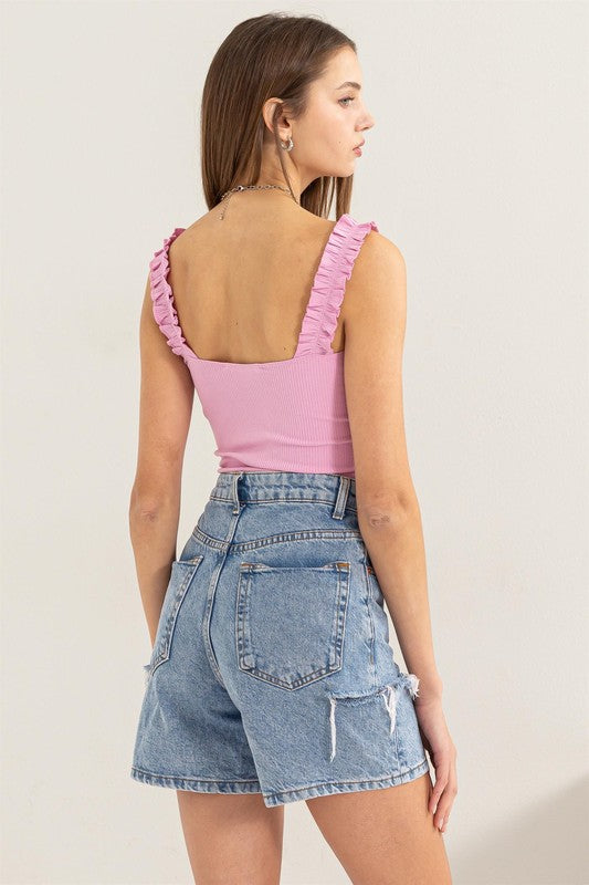 A young woman in a chic Ribbed Ruffle Strap Bodysuit and ripped denim shorts poses against a plain background.