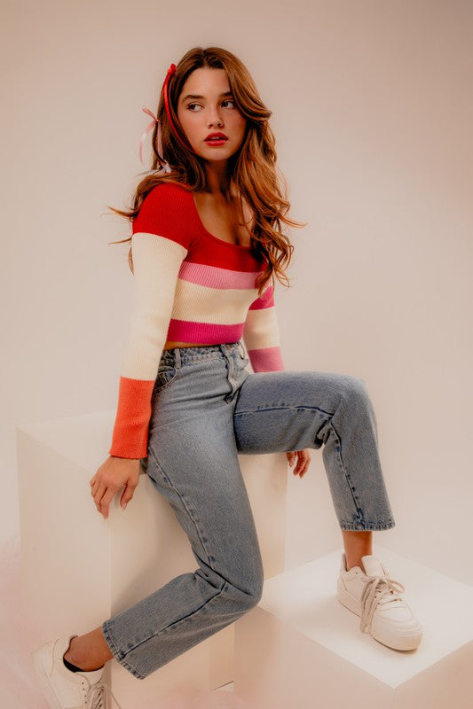 A person stands facing the camera, wearing a Long Sleeve Color Block Stripe Knit Top and a blue denim skirt. They have long hair with a white headband.