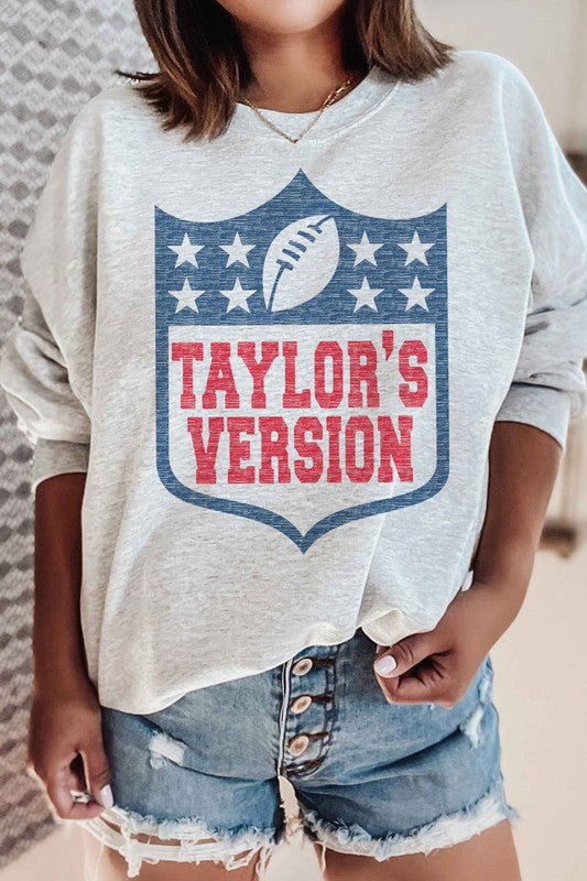 A person wearing the TAYLORS VERSION FOOTBALL GRAPHIC SWEATSHIRT, made of premium cream-colored cotton and featuring "TAYLOR'S VERSION" along with a football graphic on the front.