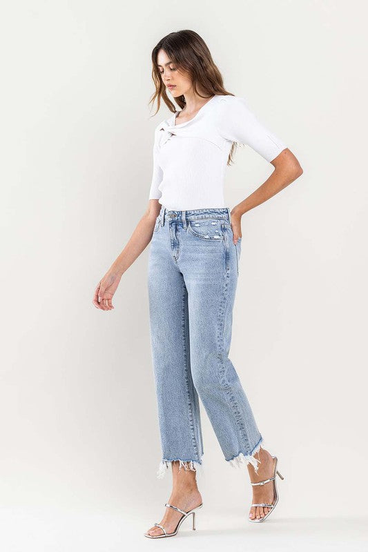 A person wearing light blue High Rise Distressed Hem Crop Dad Jeans, a white short-sleeve top, and silver open-toe heels stands against a plain background.