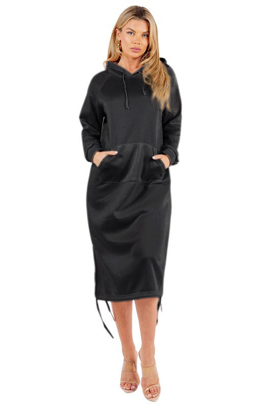 A woman is wearing a WOMEN FASHION LONG MAXI HOODIE DRESS, which is a long black sexy hoodie dress featuring a kanga pocket, drawstrings, and mid-calf length. She is standing and accessorizing her outfit with beige heels.