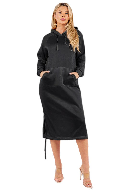 A woman is wearing a WOMEN FASHION LONG MAXI HOODIE DRESS, which is a long black sexy hoodie dress featuring a kanga pocket, drawstrings, and mid-calf length. She is standing and accessorizing her outfit with beige heels.