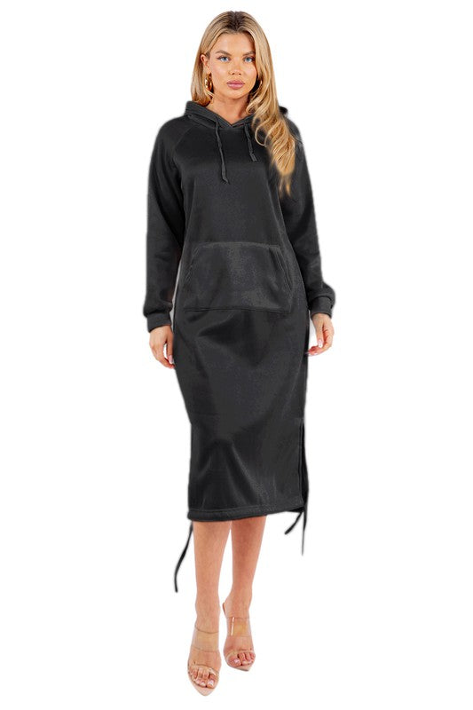 A woman is wearing a WOMEN FASHION LONG MAXI HOODIE DRESS, which is a long black sexy hoodie dress featuring a kanga pocket, drawstrings, and mid-calf length. She is standing and accessorizing her outfit with beige heels.