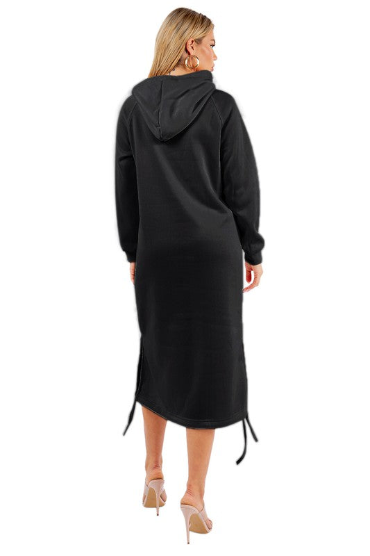 A woman is wearing a WOMEN FASHION LONG MAXI HOODIE DRESS, which is a long black sexy hoodie dress featuring a kanga pocket, drawstrings, and mid-calf length. She is standing and accessorizing her outfit with beige heels.