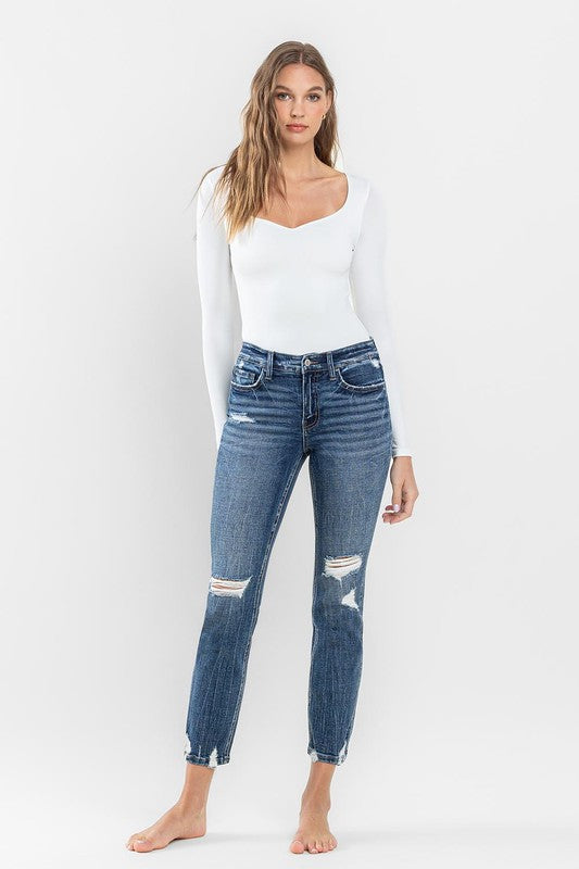 A person stands barefoot against a plain background, wearing a white long-sleeve top and the stylish Mid Rise Distressed Crop Slim Straight Jeans that perfectly capture casual elegance.