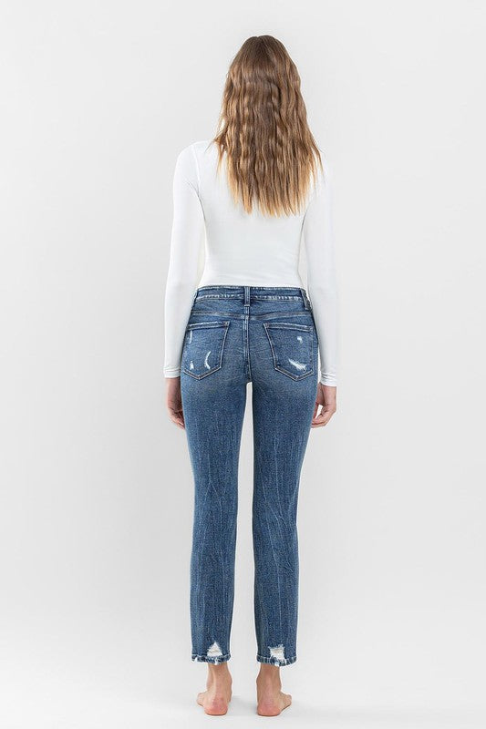 A person stands barefoot against a plain background, wearing a white long-sleeve top and the stylish Mid Rise Distressed Crop Slim Straight Jeans that perfectly capture casual elegance.