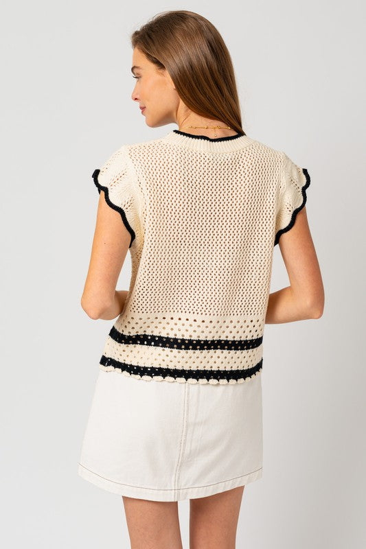 A person is wearing the Round Neck Ruffle Sleeveless Color Contrast Top, which is cream-colored with black trim and features a round neck design, paired with a white skirt, standing with hands on hips against a plain backdrop.