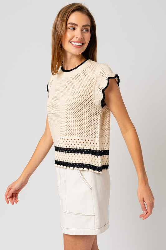 A person is wearing the Round Neck Ruffle Sleeveless Color Contrast Top, which is cream-colored with black trim and features a round neck design, paired with a white skirt, standing with hands on hips against a plain backdrop.