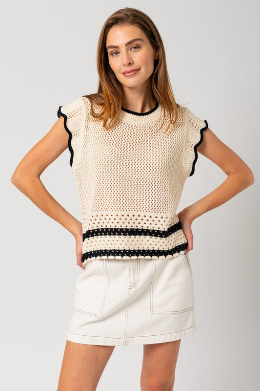 A person is wearing the Round Neck Ruffle Sleeveless Color Contrast Top, which is cream-colored with black trim and features a round neck design, paired with a white skirt, standing with hands on hips against a plain backdrop.