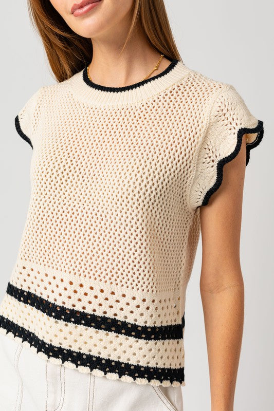 A person is wearing the Round Neck Ruffle Sleeveless Color Contrast Top, which is cream-colored with black trim and features a round neck design, paired with a white skirt, standing with hands on hips against a plain backdrop.