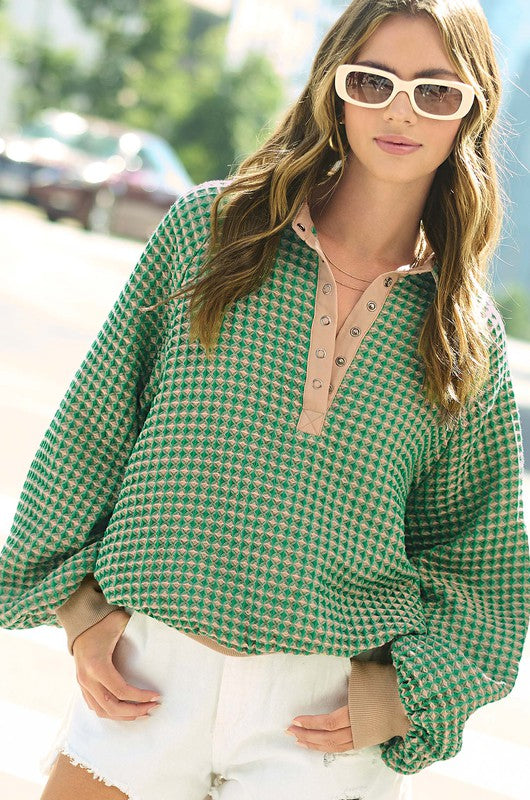 A person wearing white sunglasses, the Oversized Two-Tone Textured Long Sleeve Top with a green pattern, and white shorts stands outdoors in sunlight.