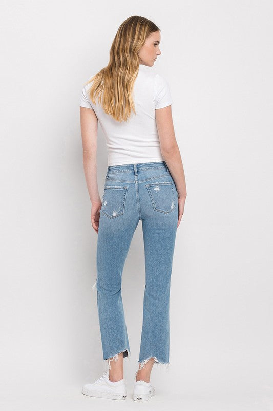 A person wearing a white T-shirt, High Rise Distressed Cropped Straight Jeans in light blue, and white sneakers stands against a plain background.