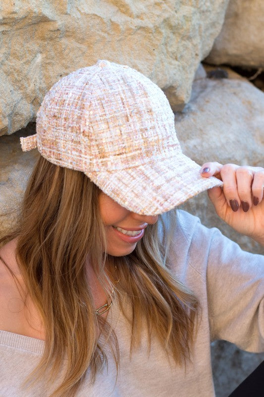 Woman smiling and tipping her Tweed Sparkle Ball Cap forward while standing near a rock face.