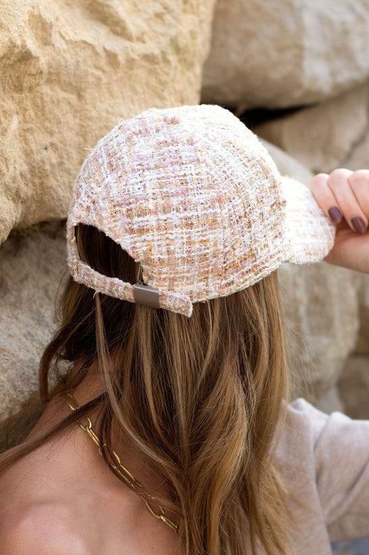 Woman smiling and tipping her Tweed Sparkle Ball Cap forward while standing near a rock face.