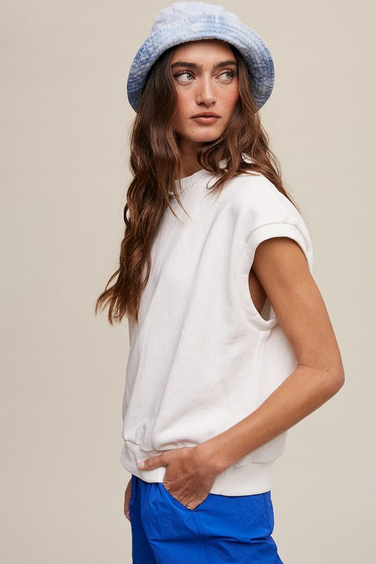 A woman stands against a neutral background, wearing the Short Sleeve Boxy Crew Neck Sweat Top in blue with ribbed detailing over a white button-up shirt.