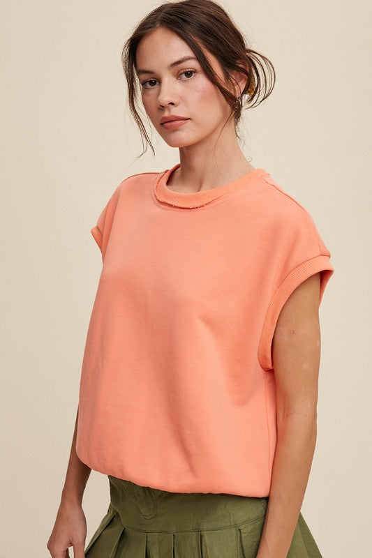 A woman stands against a neutral background, wearing the Short Sleeve Boxy Crew Neck Sweat Top in blue with ribbed detailing over a white button-up shirt.