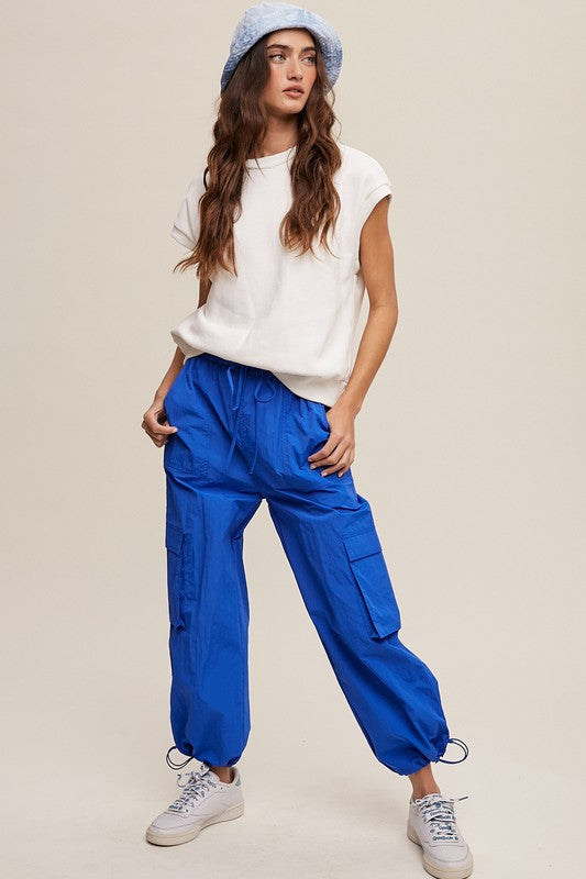 A woman stands against a neutral background, wearing the Short Sleeve Boxy Crew Neck Sweat Top in blue with ribbed detailing over a white button-up shirt.