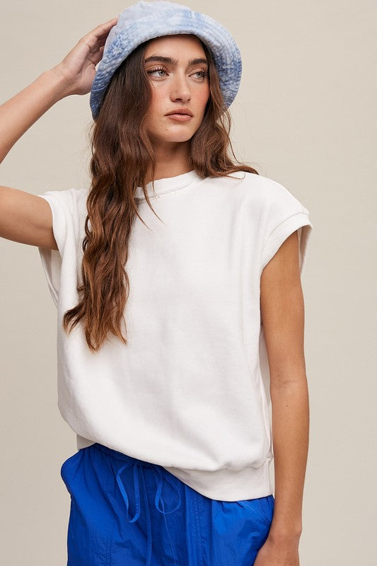 A woman stands against a neutral background, wearing the Short Sleeve Boxy Crew Neck Sweat Top in blue with ribbed detailing over a white button-up shirt.