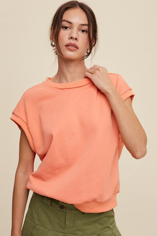 A woman stands against a neutral background, wearing the Short Sleeve Boxy Crew Neck Sweat Top in blue with ribbed detailing over a white button-up shirt.