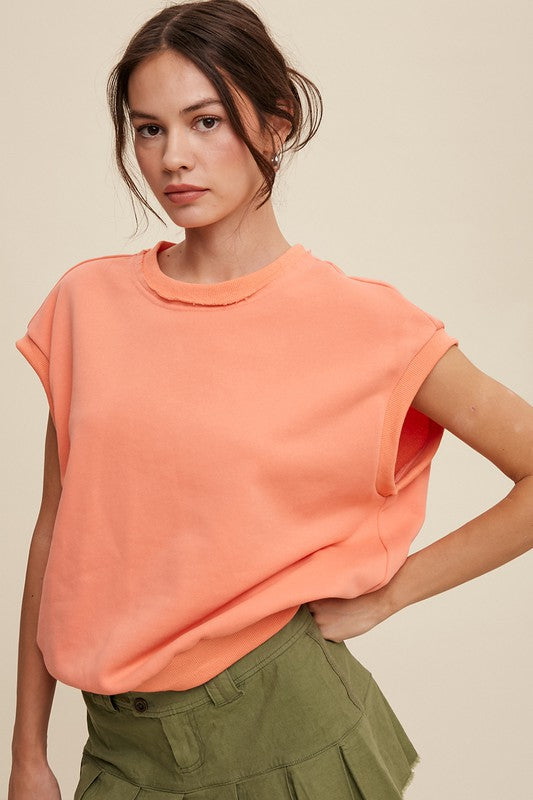 A woman stands against a neutral background, wearing the Short Sleeve Boxy Crew Neck Sweat Top in blue with ribbed detailing over a white button-up shirt.