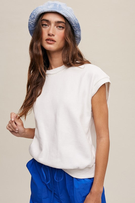 A woman stands against a neutral background, wearing the Short Sleeve Boxy Crew Neck Sweat Top in blue with ribbed detailing over a white button-up shirt.